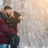 a man and a woman stand embracing in the snow and kissing
