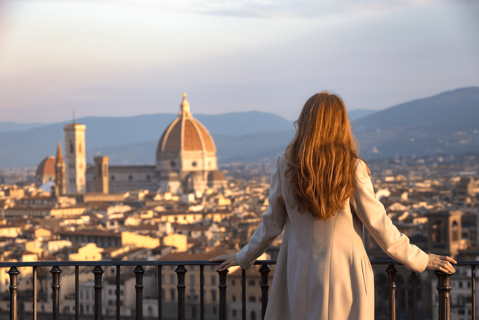 una bella donna dai lunghi capelli castani si appoggia a una ringhiera e guarda in lontananza