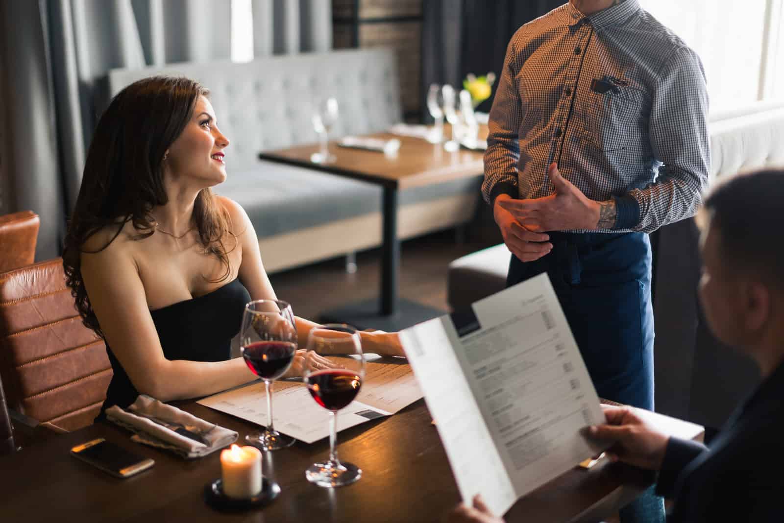 a man and a woman sit at a table and talk to a waiter