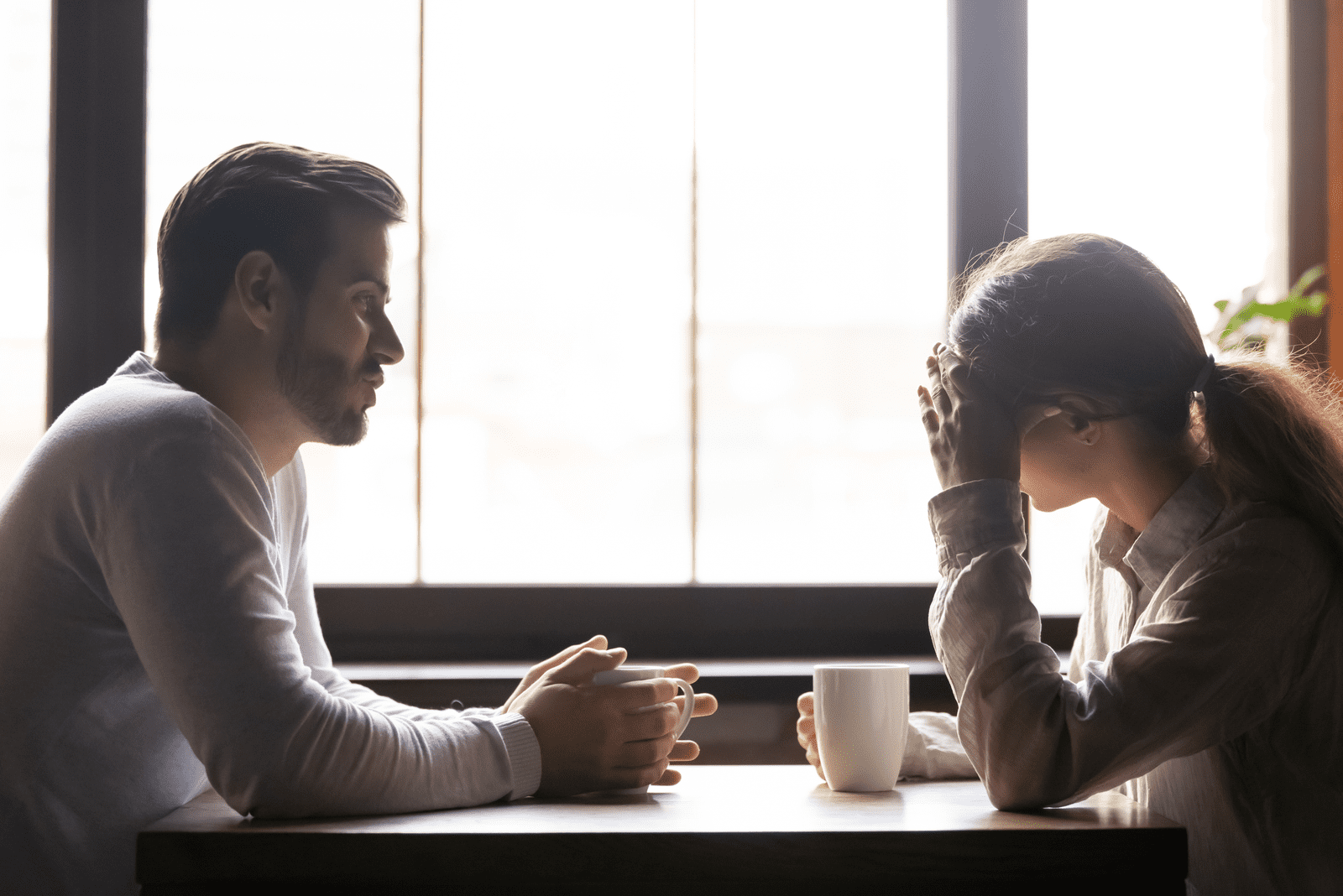 a man and a woman sit at a table in a cafe and discuss fake people