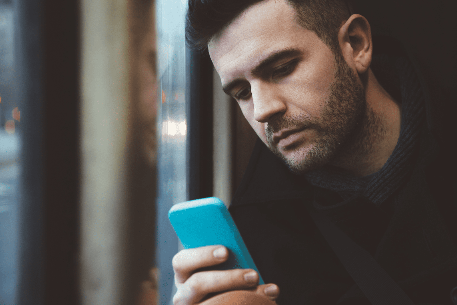 a man sits by the window and buttons on the phone