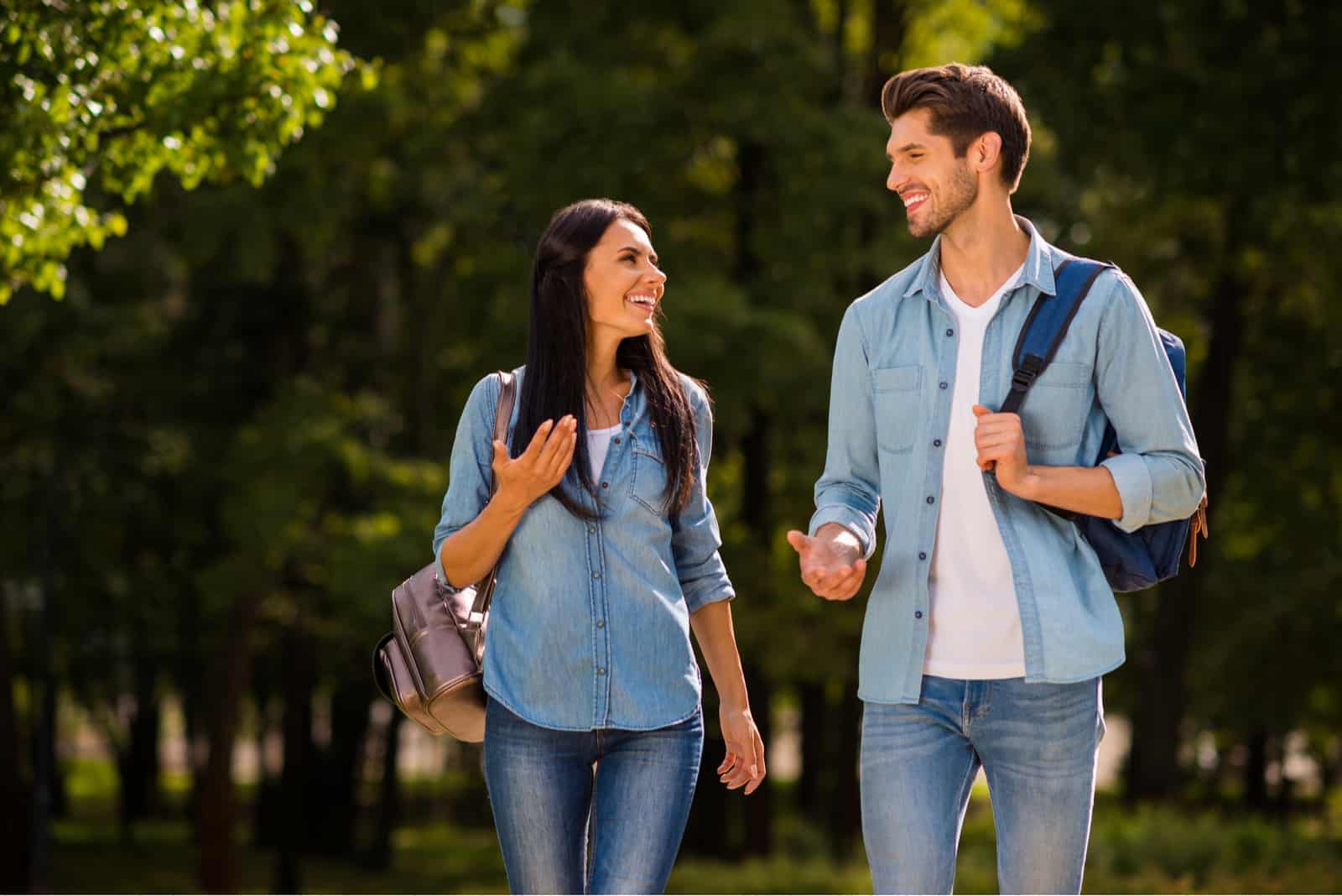 a smiling man and woman walk through the park and talk