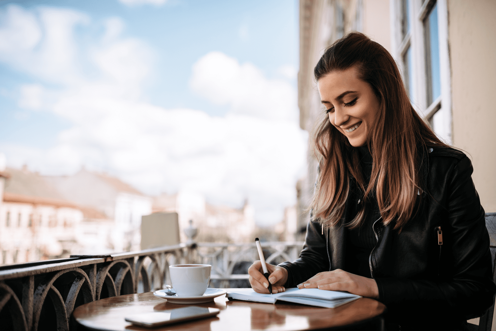 a smiling woman sits at a table and writes