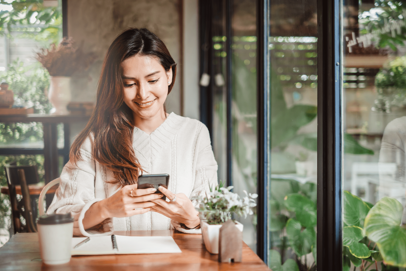 una donna sorridente seduta in un caffè a scrivere al telefono