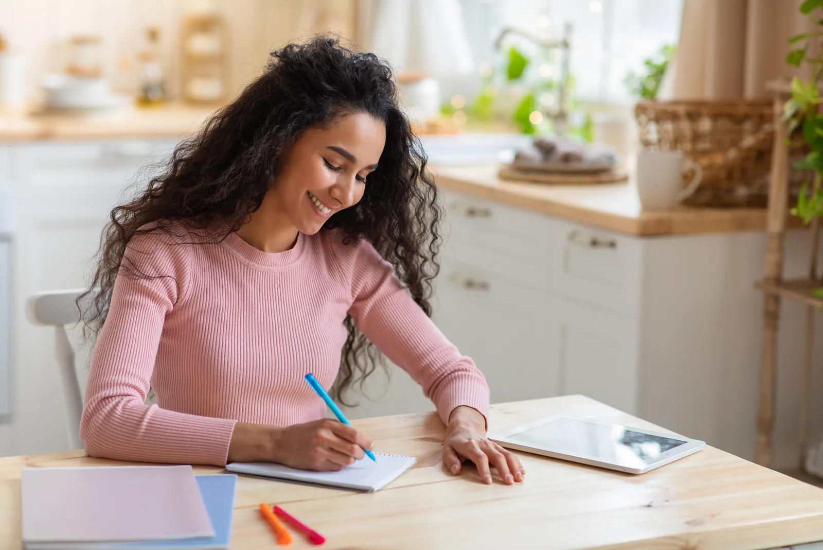 a smiling woman with frizzy hair sits at a table and writes
