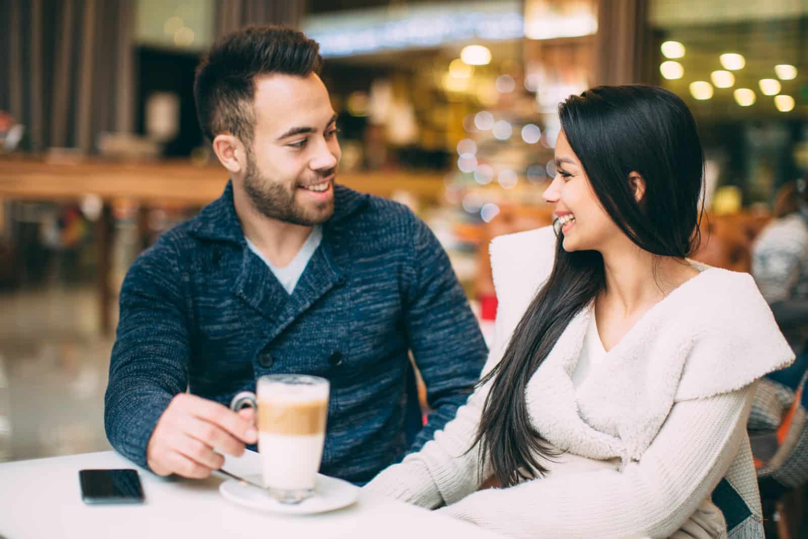 a smiling woman with long black hair is sitting in a cafe with a man