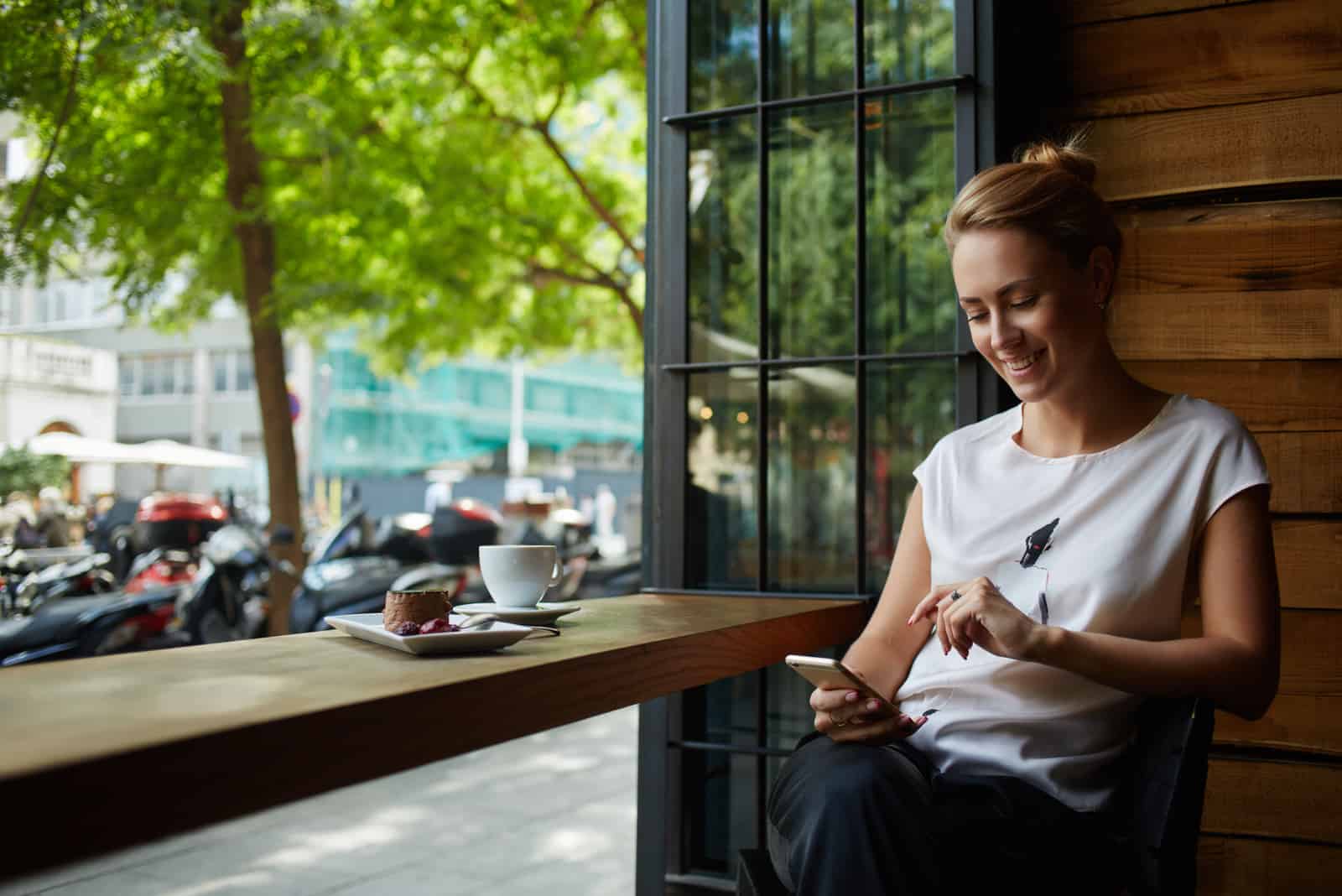 a woman with tied hair is sitting in a cafe holding a phone in her hand