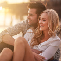 una pareja sonriente y cariñosa se abraza sentada en la playa