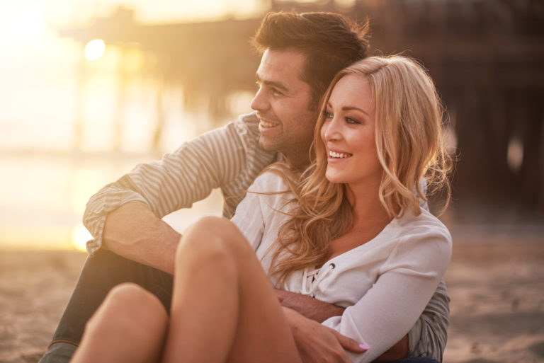 a smiling loving couple embracing sitting on the beach