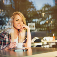 a smiling woman sitting at a table drinking coffee