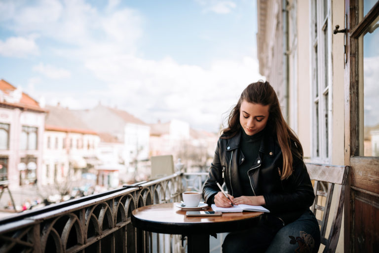 a woman with long brown hair sits at a table and writes