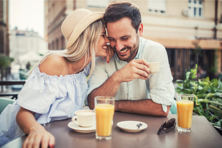 a smiling woman with a hat on her head leaning on a man's shoulder