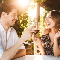 a smiling man and woman sit and drink wine