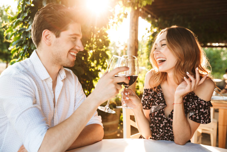 a smiling man and woman sit and drink wine