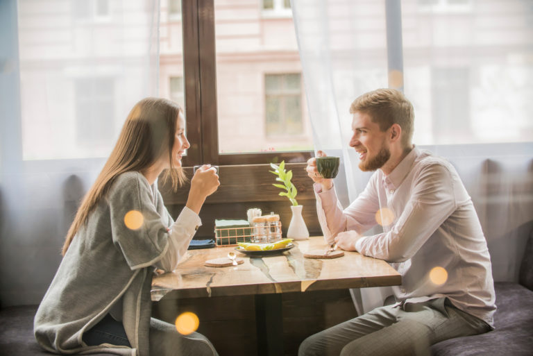 a smiling man and woman sitting at a table having coffee talking