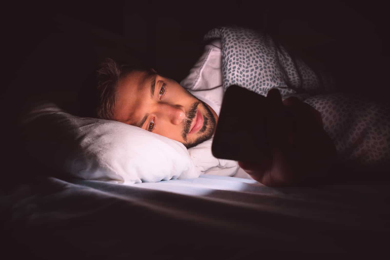 um homem bonito deitado na cama e a carregar no telefone