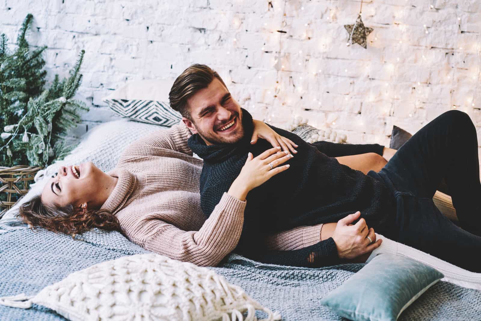 a smiling man and woman lie on the bed