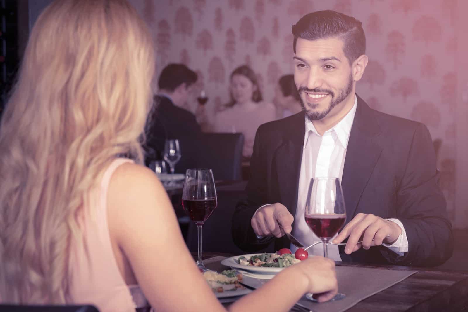 a smiling man sits at a table with a woman and eats