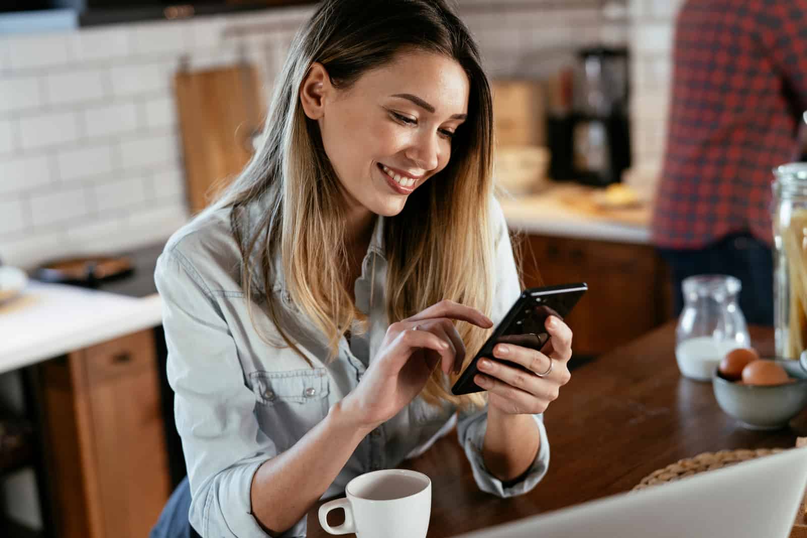 a smiling woman sitting at a table and pressing a phone