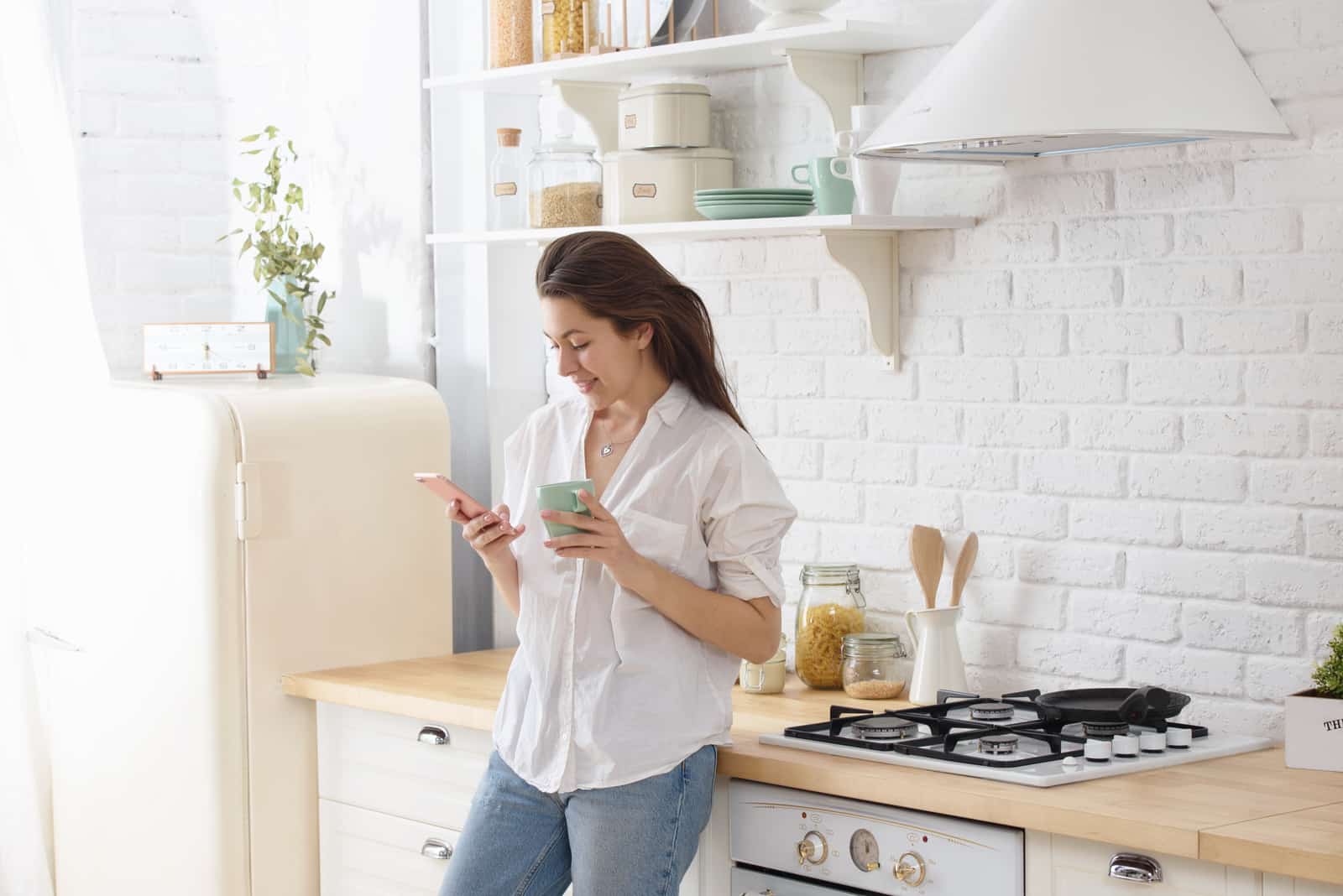 a smiling woman standing in the kitchen and pressing a phone