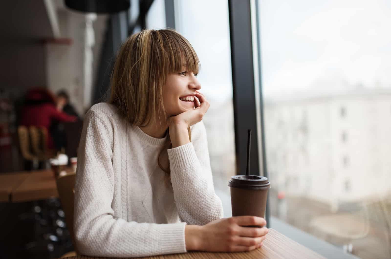 rapariga feliz a beber café e a pensar no que fazer quando um homem de Touro sente a sua falta