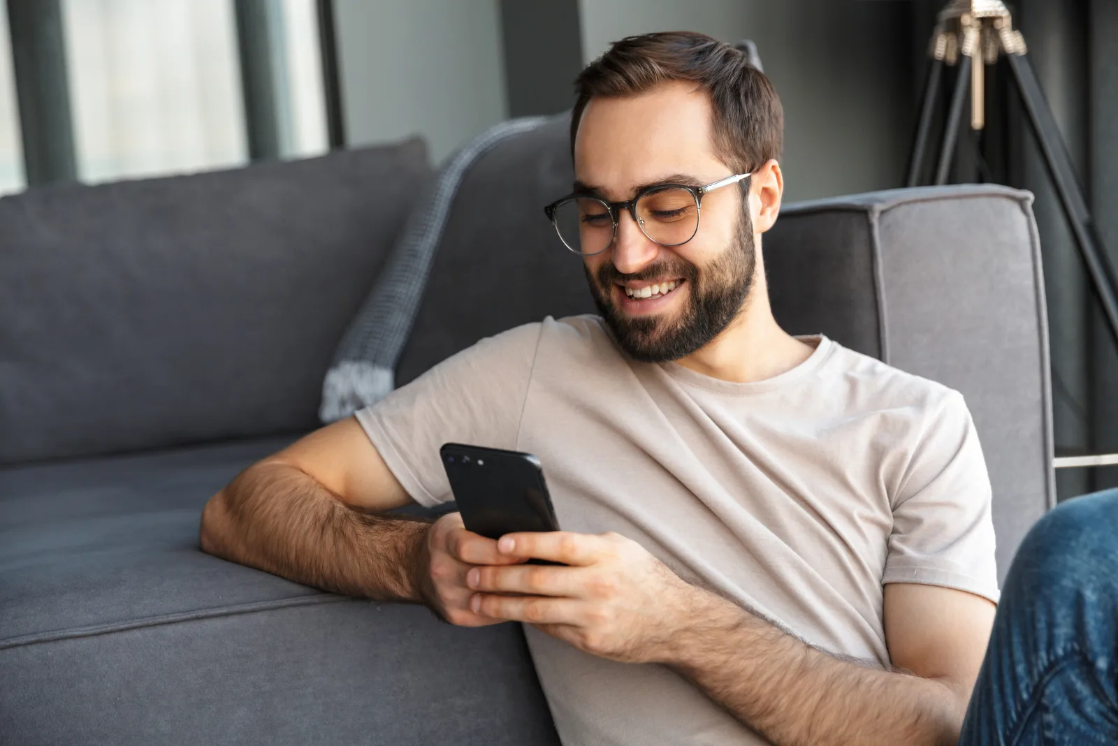smiling man leaning on couch button on phone