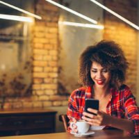 uma mulher sorridente senta-se a uma mesa e segura um telemóvel na mão