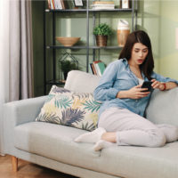 a woman with long black hair is sitting on the couch holding a phone in her hand