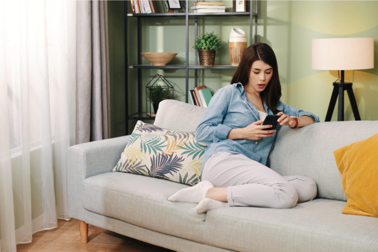 a woman with long black hair is sitting on the couch holding a phone in her hand