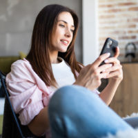 a black haired woman sits in a chair holding a phone in her hand