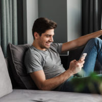 handsome young man sitting on the couch and looking at mobile phone