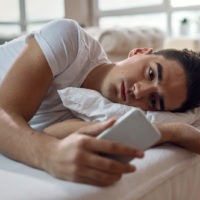 man lying in bed and staring at his phone
