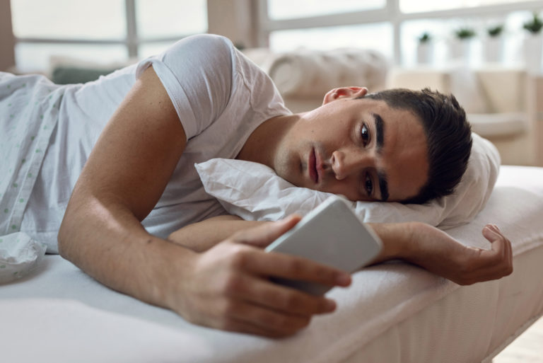 man lying in bed and staring at his phone