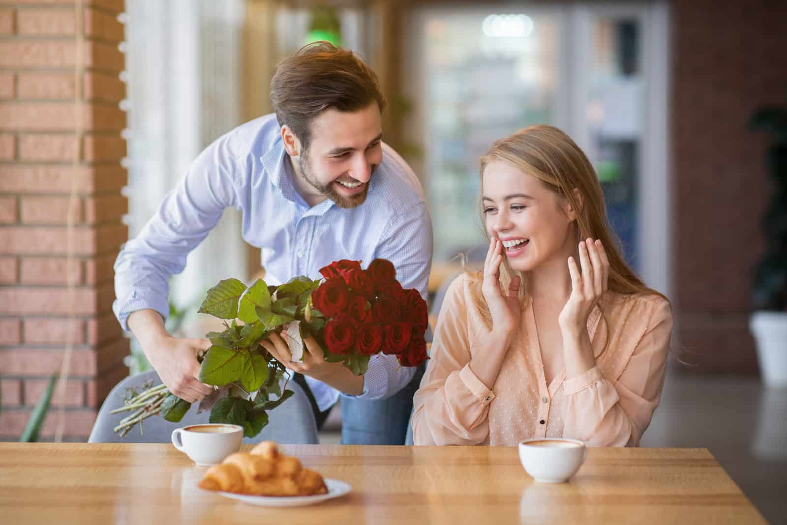 a beautiful man surprised a woman sitting in a cafe with a bouquet of roses