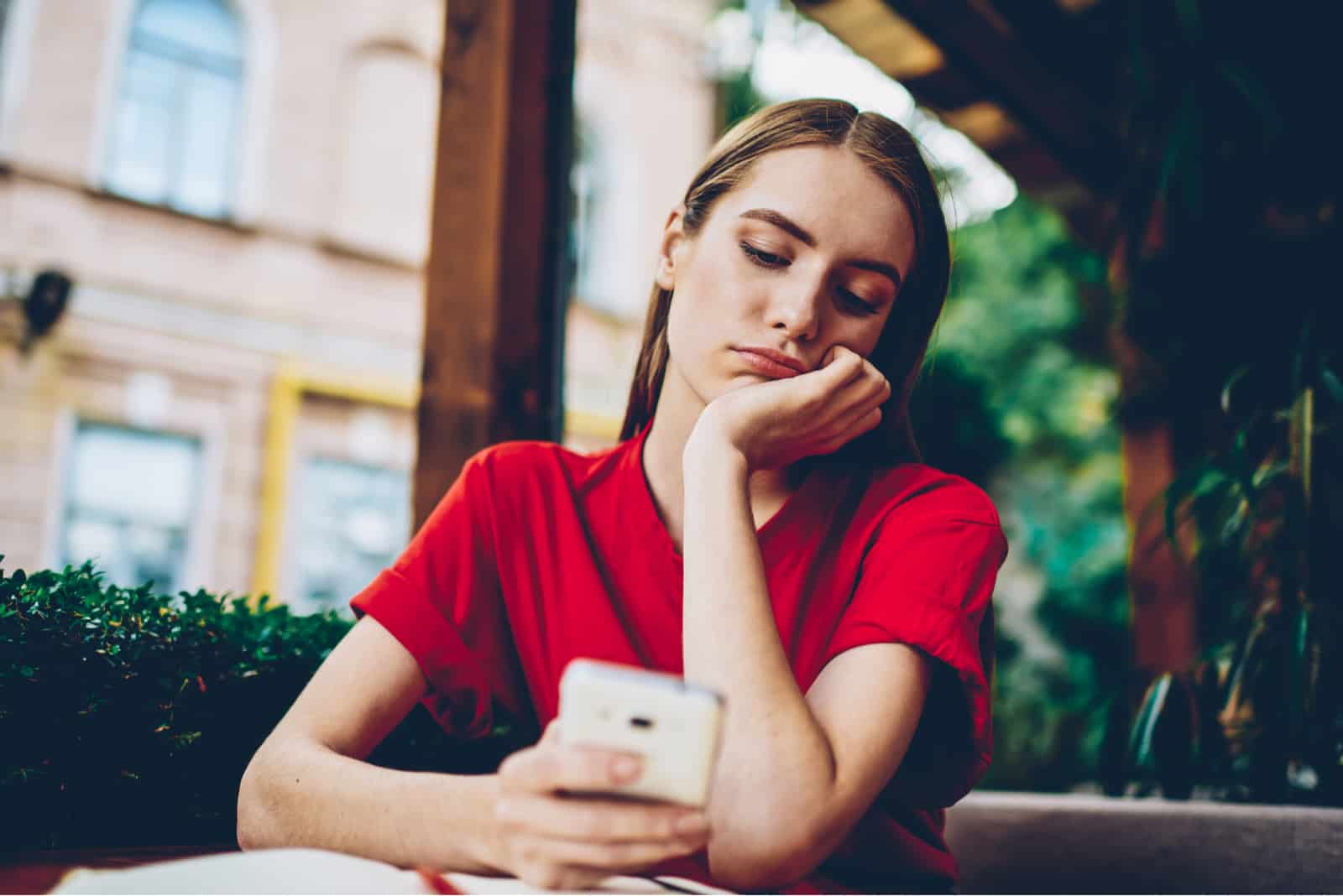 a disappointed woman sitting at a table holding a cell phone in her hand