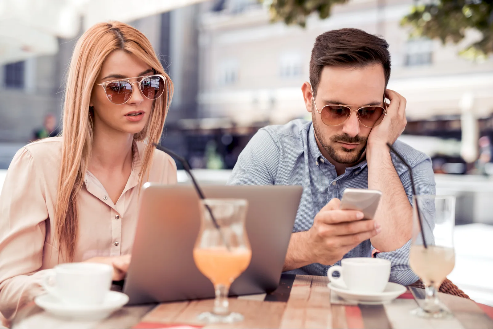 a man and a woman sit while he types on the phone and she on the laptop