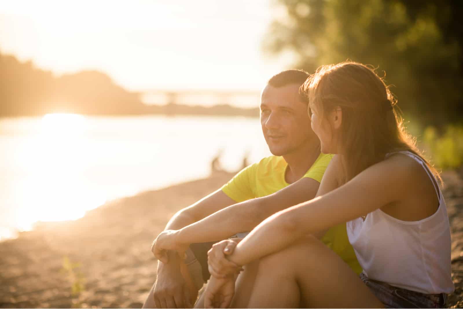 a man and a woman sitting on the beach and talking