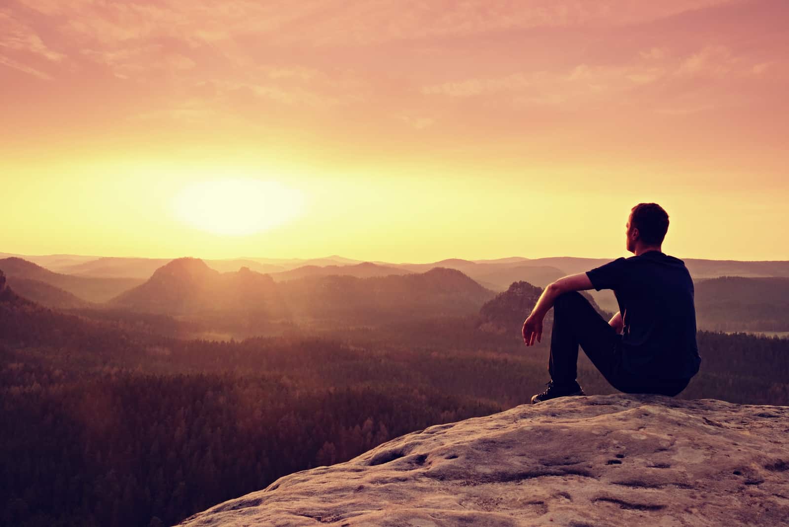 a man sits on a rock and looks into the distance