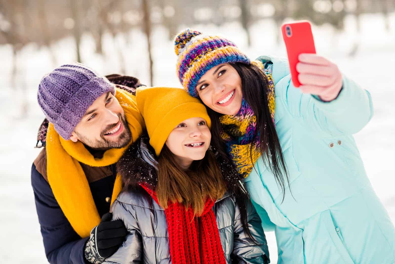 a smiling loving couple taking a picture with a child in the snow