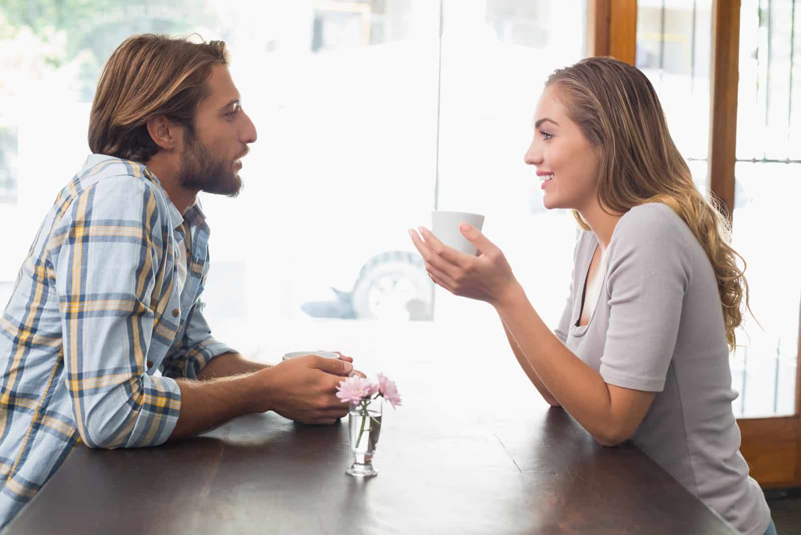 a smiling woman sits at a table with a salt shaker in her hand and talks to a man