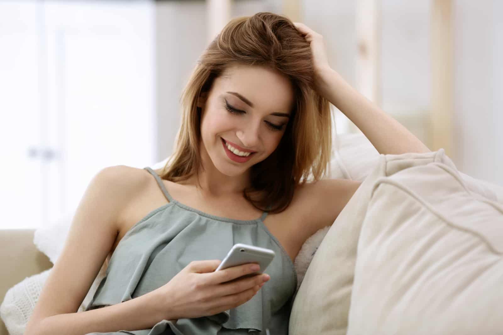 a smiling woman sits on the couch and buttons on the phone