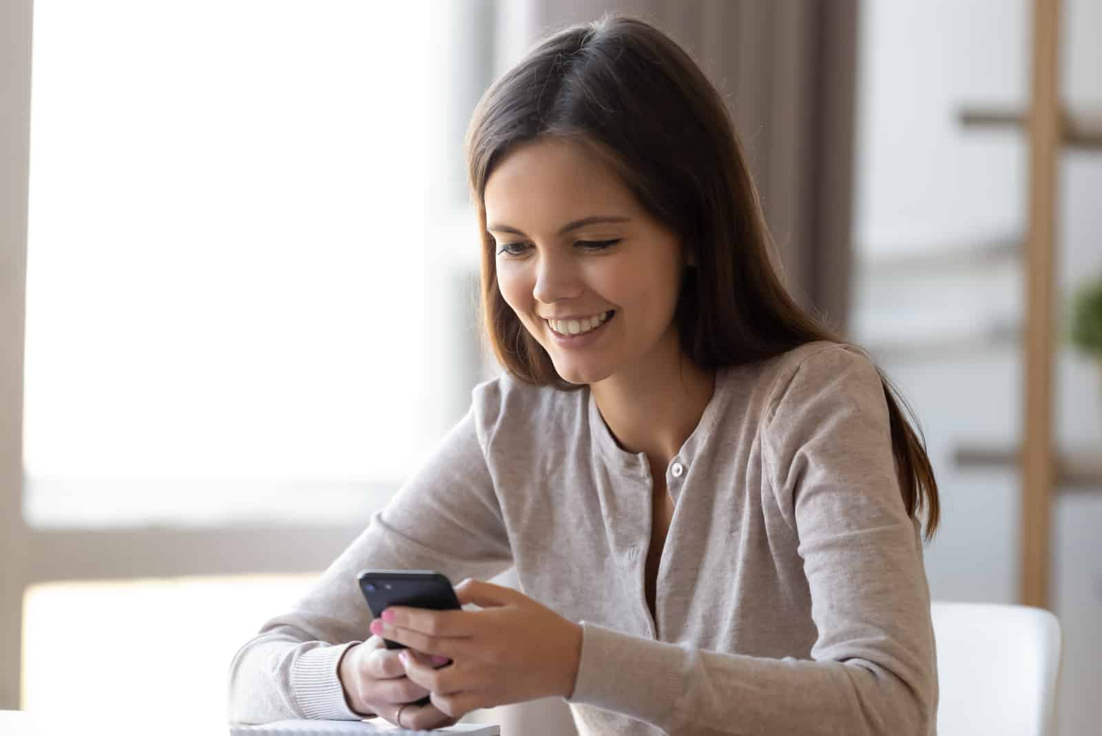 a smiling woman sitting at a table and pressing a phone