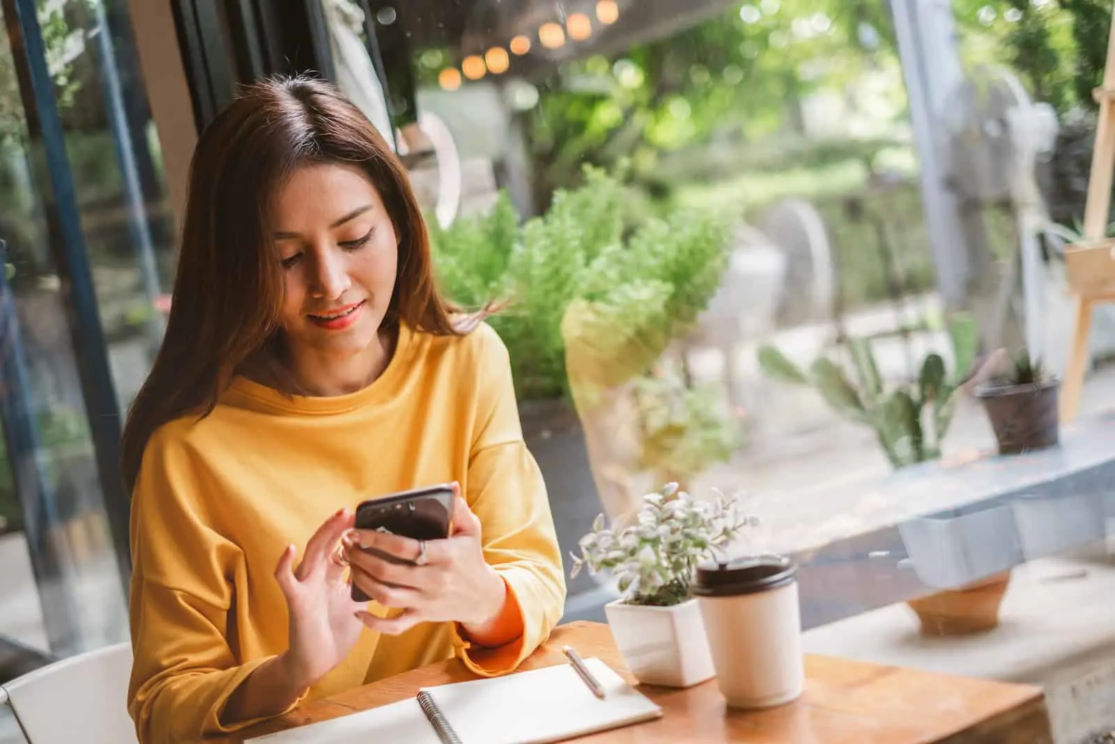 a smiling woman sitting at a table and pressing a phone