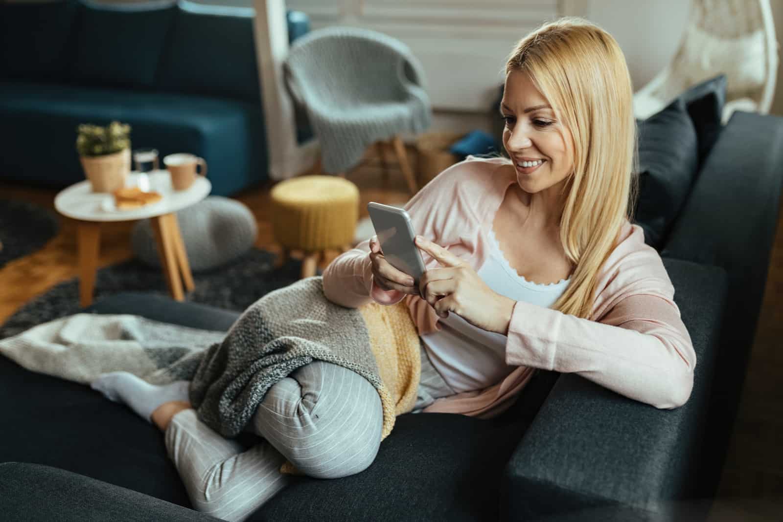 a woman with long blonde hair sits on the couch and holds the phone in her hand