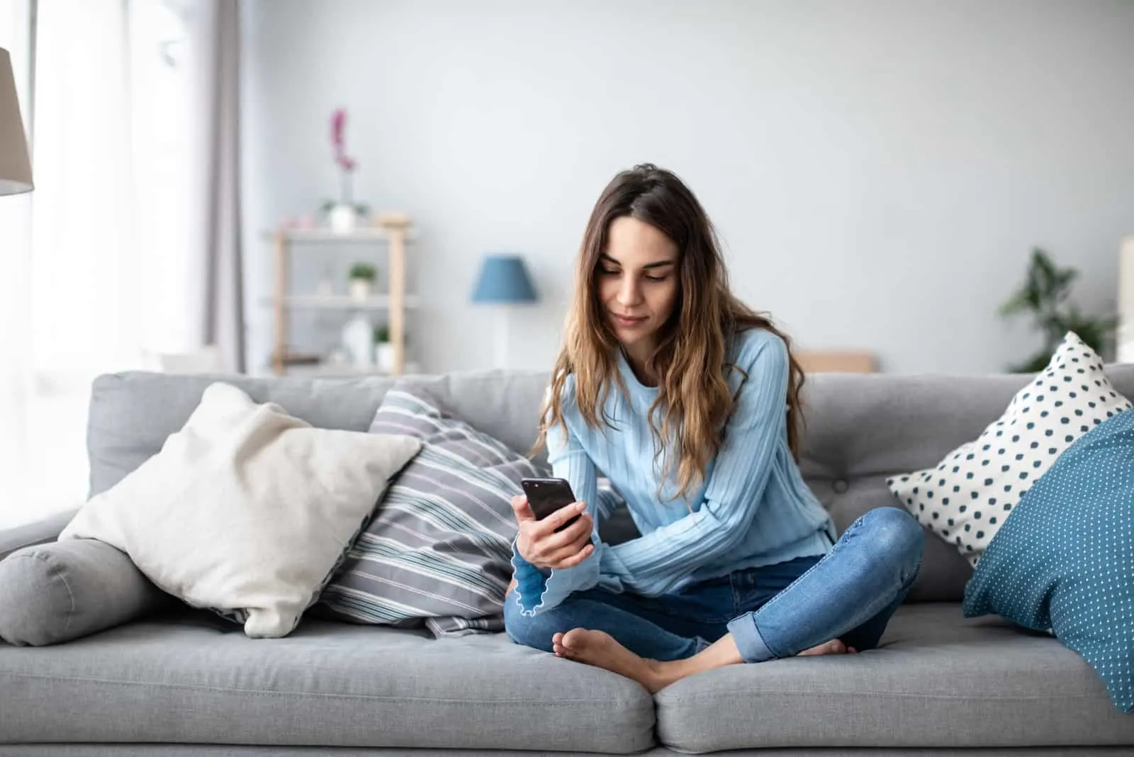 a woman with long brown hair is sitting on the couch holding a phone in her hand