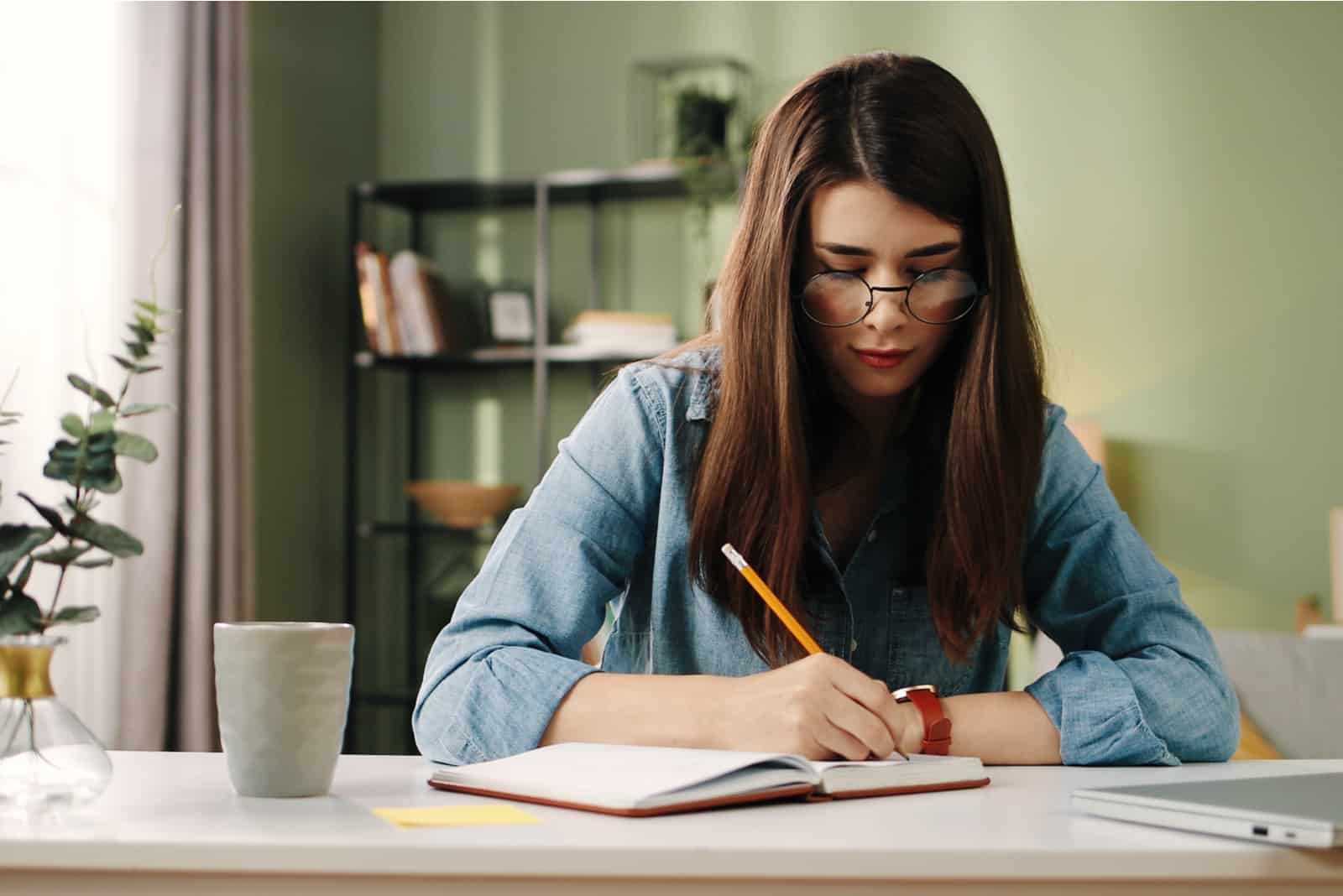 a woman with long brown hair sits at a table and writes