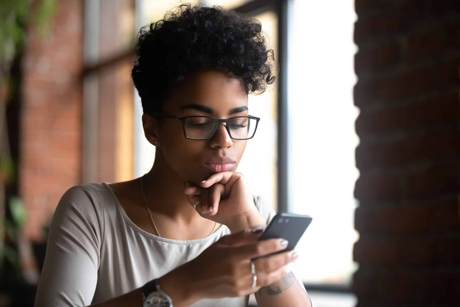 an imaginary short-haired woman sits at a table holding a cell phone in her hand