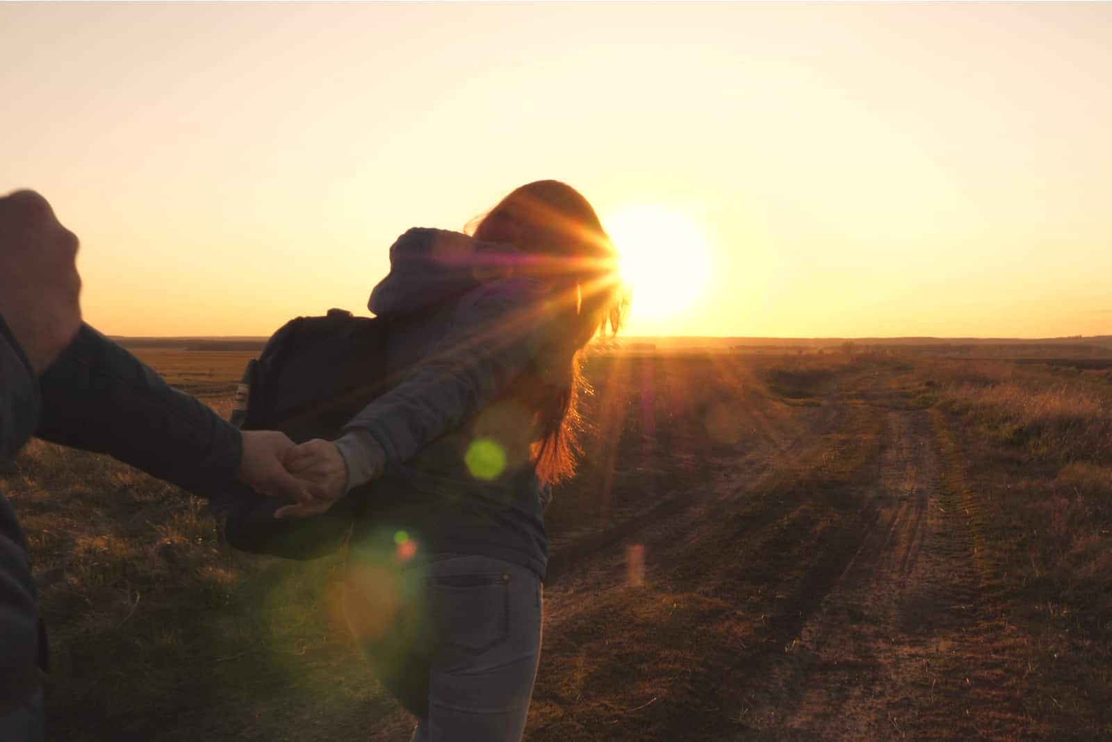couple holding hands walking towards sunset