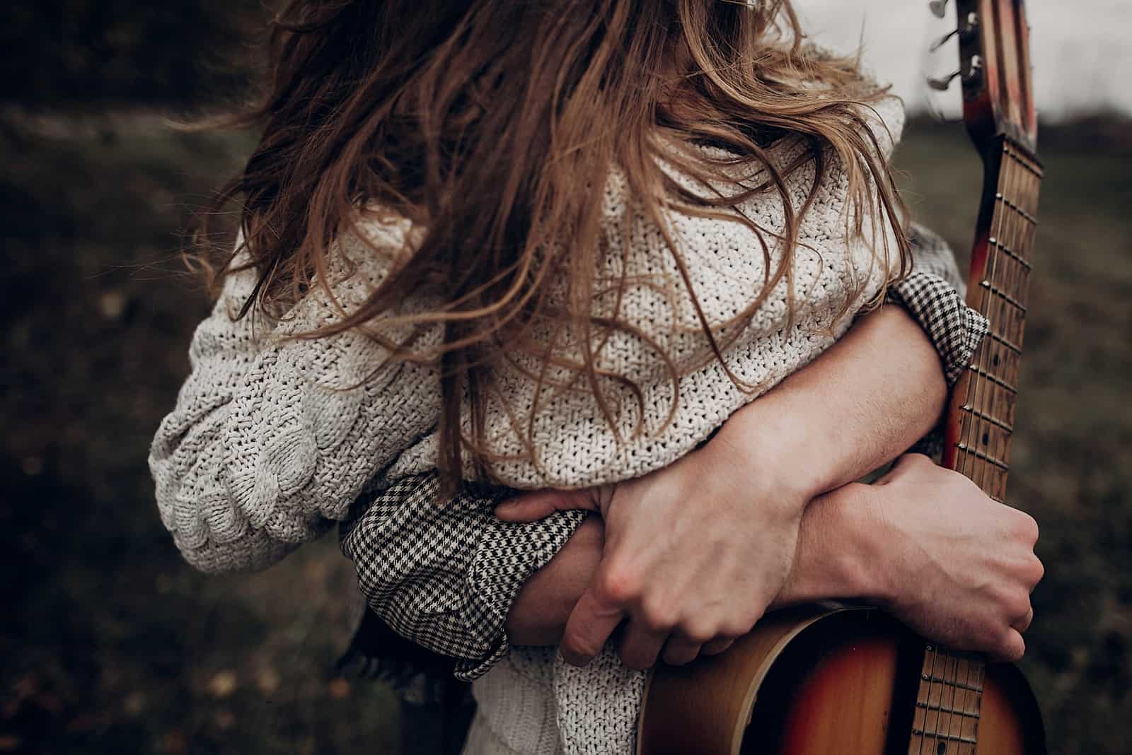 man hugging a woman while holding a guitar