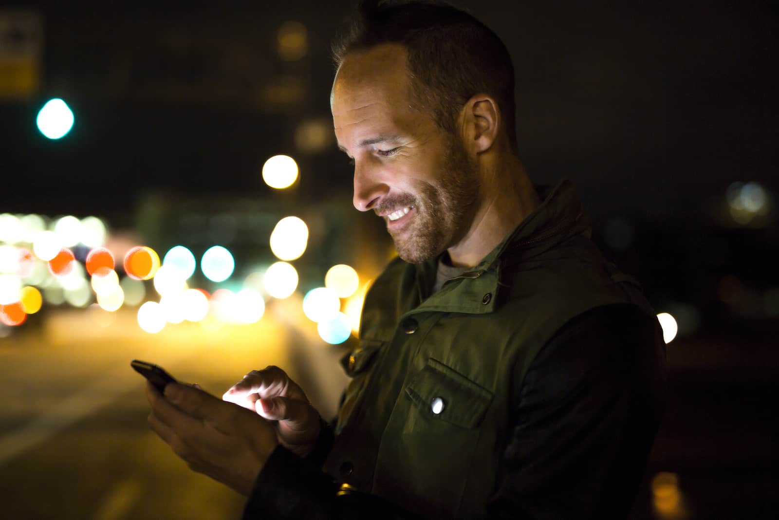 uomo durante una serata fuori casa che legge i messaggi sul suo telefono